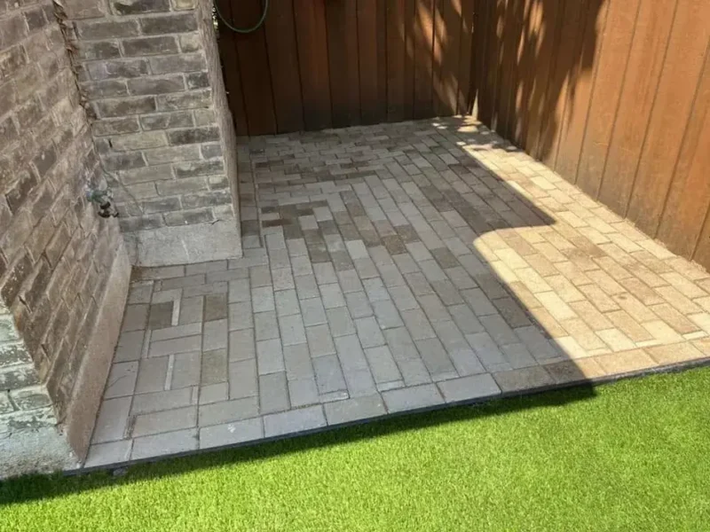 Paver pad beside artificial turf in a fenced side yard