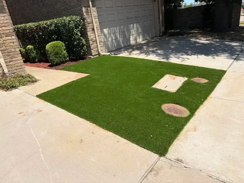 Artificial turf beside a garage and driveway, with utility covers accessible