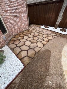 Paver patio beside a white rock bed with a tree and accent boulders