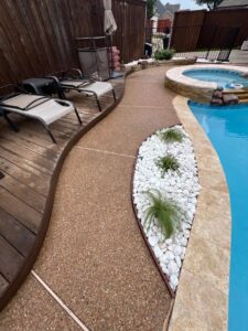 White rock bed with ornamental plants beside a pool and patio