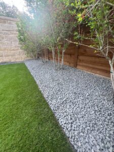 Artificial turf bordered by metal edging and a planted gray rock bed