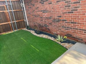 Artificial turf beside a curved Benda Board flowerbed with light and dark rocks and plants