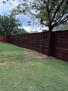 Horizontal wood fence enclosing a backyard lawn beneath an established tree