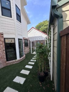 Artificial turf side yard with a concrete paver pathway leading to a covered patio