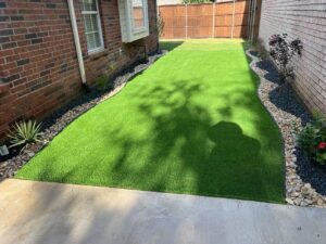 Finished artificial turf side yard with Benda Board flowerbed edging, multicolored rocks and plants